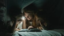 Seorang ibu sedang membacakan buku cerita rakyat bergambar kepada anaknya di dalam kamar yang hangat untuk mempererat keakraban emosional sebelum tidur.