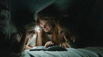 Seorang ibu sedang membacakan buku cerita rakyat bergambar kepada anaknya di dalam kamar yang hangat untuk mempererat keakraban emosional sebelum tidur.